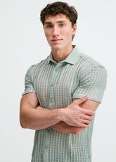 A man with curly hair wears a short-sleeve ocean-colored button-down shirt with an open knit texture and rib collar.