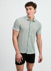 A male model wearing an ocean-colored open-knit short-sleeve button-down shirt with a rib collar and black shorts.