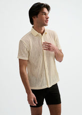 A model wears a ST33LE off-white open knit short-sleeve button-down shirt with a rib collar and black shorts.
