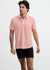 A man models a pink ST33LE open-knit short-sleeve button-down shirt with a ribbed collar, paired with black shorts.