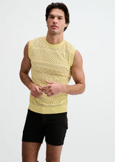 A man wearing a cream-colored pointelle open knit vest tank top and black shorts against a white background.