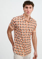 A man wearing a short-sleeve button-down shirt with a geometric spice and sand pattern against a plain background.