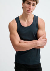A man with his arms crossed wears a dark mariner performance tank top.