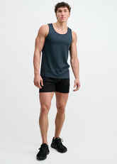 A model stands in a blue textured stretch mesh performance tank and black shorts against a plain white backdrop.