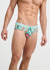 A man models ST33LE teal swim briefs featuring a colorful multi drips print and an adjustable drawstring waistband.