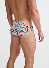 Rear view of a man wearing ST33LE teal swim briefs featuring a multi-color swirl pattern against a plain background.