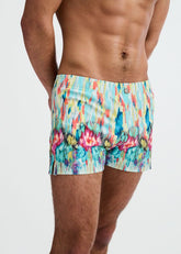 Torso view of a model wearing ST33LE teal swim shorts with a multicolored paint-drip print against a white background.