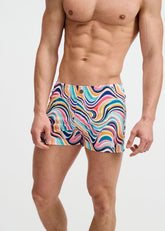 An athletic man wears ST33LE Swirls Printed Swim Shorts in teal and multi-color wavy psychedelic stripes.