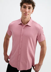 A man wearing the ST33LE Stretch Knit Shirt in carnation pink, featuring short sleeves and a button-down collar.