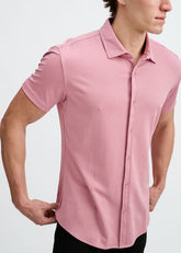A man wearing a short-sleeve carnation pink button-down shirt against a plain white background.