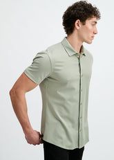 A man wearing a short-sleeve button-down stretch knit shirt in light laurel green against a plain background.