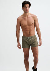 Shirtless male model wearing ST33LE combat green gym shorts with a drawstring waist, standing against a white backdrop.