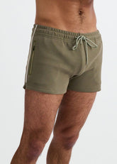 A man wears ST33LE combat green gym shorts with contrast piping, a zippered pocket, and an elastic drawstring waist.