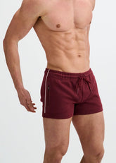 A muscular man models ST33LE wine gym shorts with contrast piping and a drawstring waist against a white background.