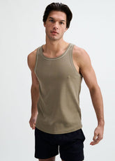 A male model wearing a ranger green ribbed ringer tank top with white piping detail, paired with black shorts.