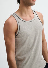 A man wearing a grey ribbed stretch ringer tank top with black piping detail along the neckline and armholes.