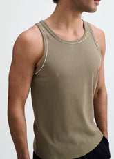 A man wearing a ribbed ranger green tank top with contrasting white piping along the neckline and armholes.
