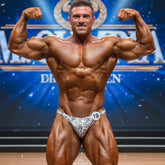A muscular man wearing metro malewear posingwear white and gray snake skin competition briefs with number 18 pinned