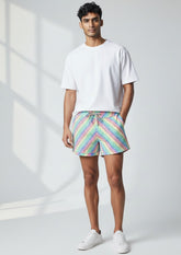 Man wearing a white t-shirt and Tulio Swimwear rainbow dots linen texture shorts, standing against a white wall.