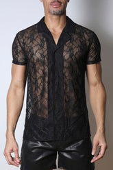 A model wearing a black lace short-sleeve button-down shirt with a collar and black leather shorts.