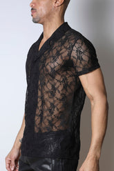 A model wearing Timoteo Windsor black lace short-sleeve button-down shirt and black pants.