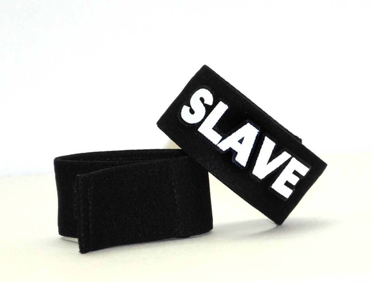 Black fabric cock ring with a "SLAVE" patch in bold white lettering, featuring a hook-and-loop closure.