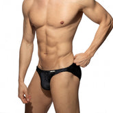 A muscular man wearing Addicted black mesh swim bikini briefs against a white background.