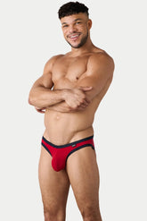 A smiling male model poses in AWRY Menswear red Aura briefs with black trim.