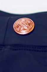 A copper-toned circular button with an intricate interlocking design on dark navy fabric of bondi short