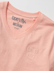 A soft peach-colored cotton born fly v-neck tee with subtle logo embroidery on the chest and brand tag neckline