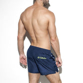 Back view of a man wearing navy blue ES Collection board shorts with a yellow logo on the back pocket.