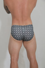 Black swim brief with a repeating white monogram pattern designed for stylish beachwear use