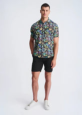 A man wearing a floral lightweight linen tencel short-sleeved shirt with a multicolored pattern on a dark background