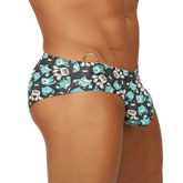 Black gigo comics swimbrief swim trunks with teal and white cartoon monsters and a metallic ring waistband accent