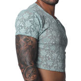 Sheer aqua blue floral lace crop top with short sleeves and a crew neck, worn by a man with arm tattoos.