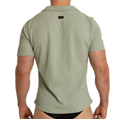 A men’s short-sleeved polo shirt in textured light sage green fabric with ribbed pattern and black collar tag back view