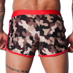 Short camo-print swim trunks with a wide red waistband and red piping trim along the leg openings.