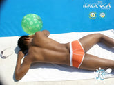 Orange swim trunks with white trim from icker sea cheeky mini bikini swimwear lying on towel beside pool