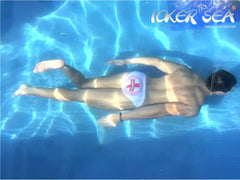 A man wearing icker sea lifeguard micro slip bikini swimwear in white with a red cross emblem floats underwater in a pool