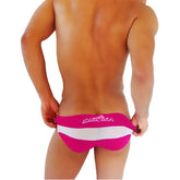 Bright pink and white striped men’s swim trunks with transparent panel and joker & sea branding in fuchsia