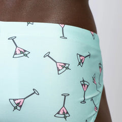Mint green martini swim brief with playful pink martini glass pattern and olive garnishes in black outline