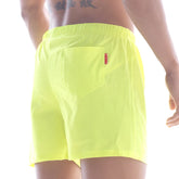 Bright neon yellow metro male wear flexible swim trunks with a small red tag on the back pocket shown from behind