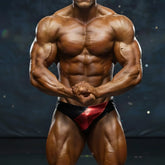 A muscular bodybuilder wearing MetroMaleWear MetroMuscleWear red and black competition briefs with metallic red accents