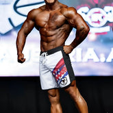 White and black MetroMuscleWear IFBB Pro mens physique board shorts with red white and blue star stripe and black bull logo