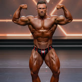 A muscular man flexing in black and red striped metroMuscleWear stripe competition briefs on stage