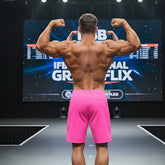 A muscular man displays the back side of metroMalewear physique board shorts in neon pink on stage, highlighting muscle definition