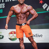 MetroMaleWear physique board short orange with black waistband and drawstring featuring a shield logo on the lower right leg