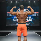 A muscular man shows the back of metro malewear physique board short orange-black with black waistband on stage