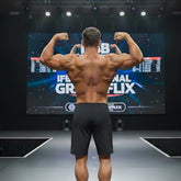A muscular man shows the back side of black MetroMaleWear Physique board shorts with stripe detailing on stage