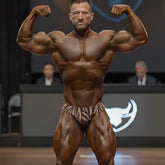 A muscular man flexing on stage wearing MetroMaleWear gold zebra posing suit in brown and beige zebra-striped briefs